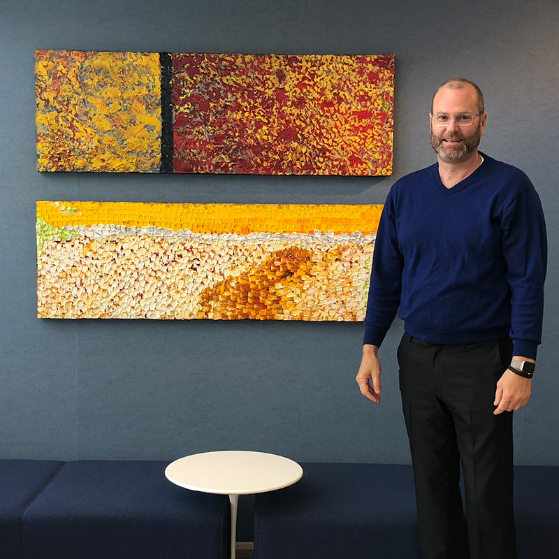 Artist Marc stands with three of his colorful abstract paintings hanging on a wall at PayPal HQ.