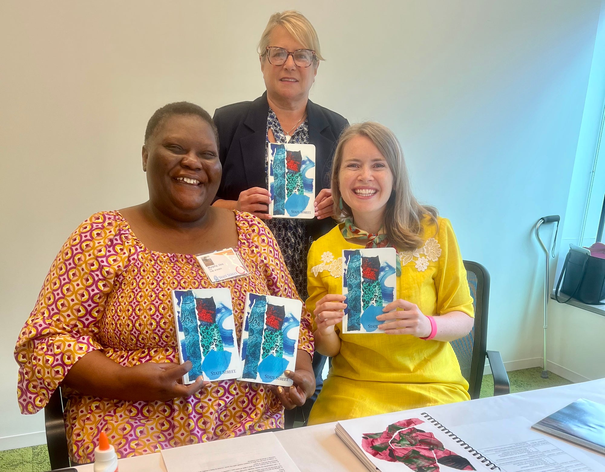 Lisa Murphy (left), Karen Faison (center), and Liz Powers (right) holding ArtLifting x State Street notebooks featuring Lisa Murphy's artwork, taken after Lisa's virtual workshop.