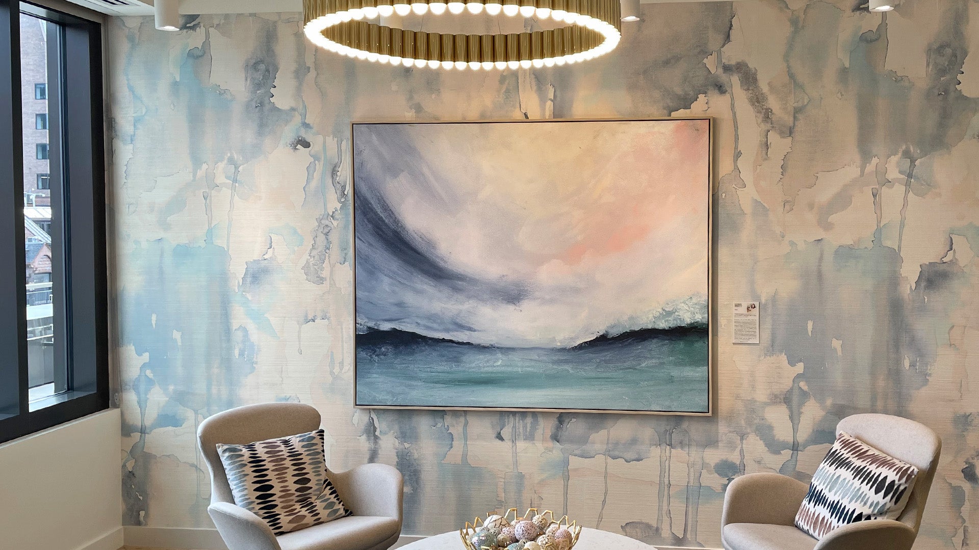 Vasta by Elizabeth Shanahan hangs on a decorative wall in a posh seating area with a chandelier above it.