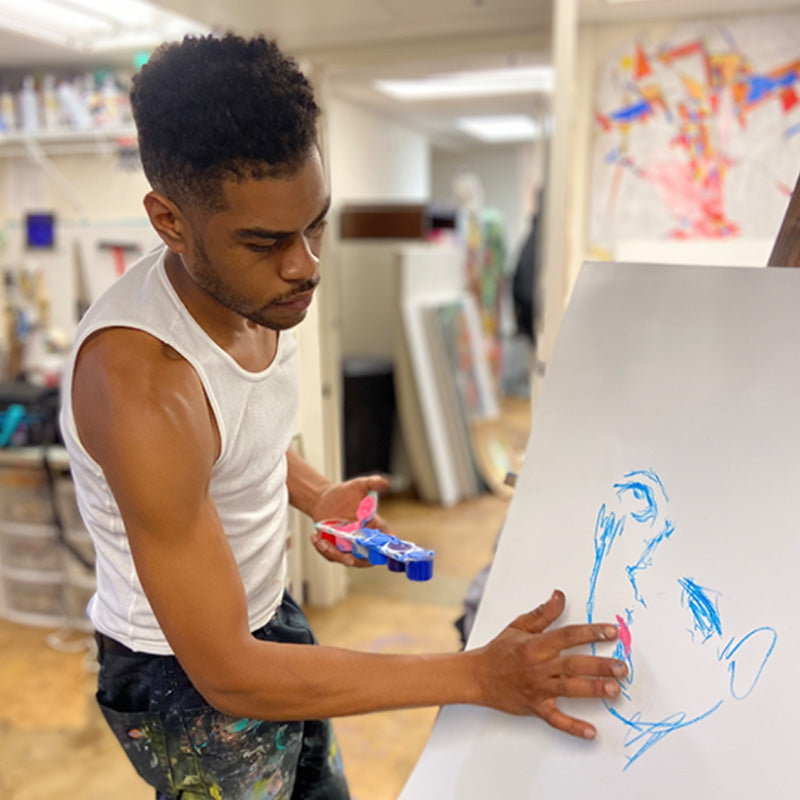 Artist Justin Ellis applies paint to paper with his fingers in an art studio.